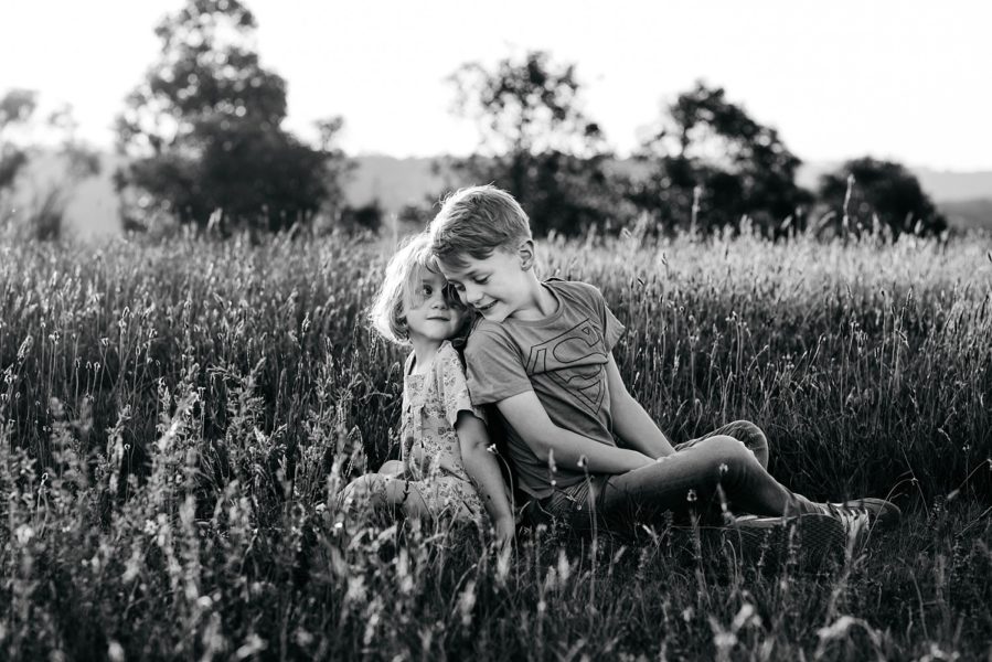 A boy and a girl are sitting in the grass leaning back on each other, the image is in black and white