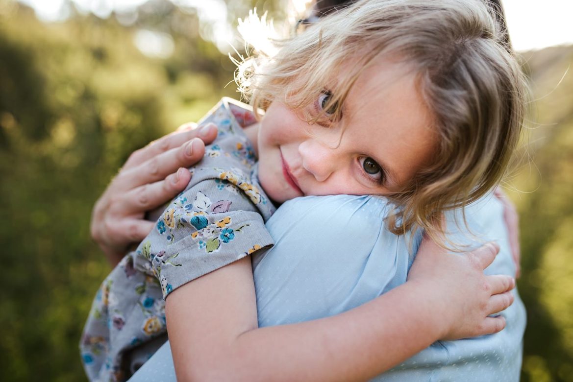A close up of a young girl leaning against her mothers' shoulder she is clinging tight and they are both wearing blue