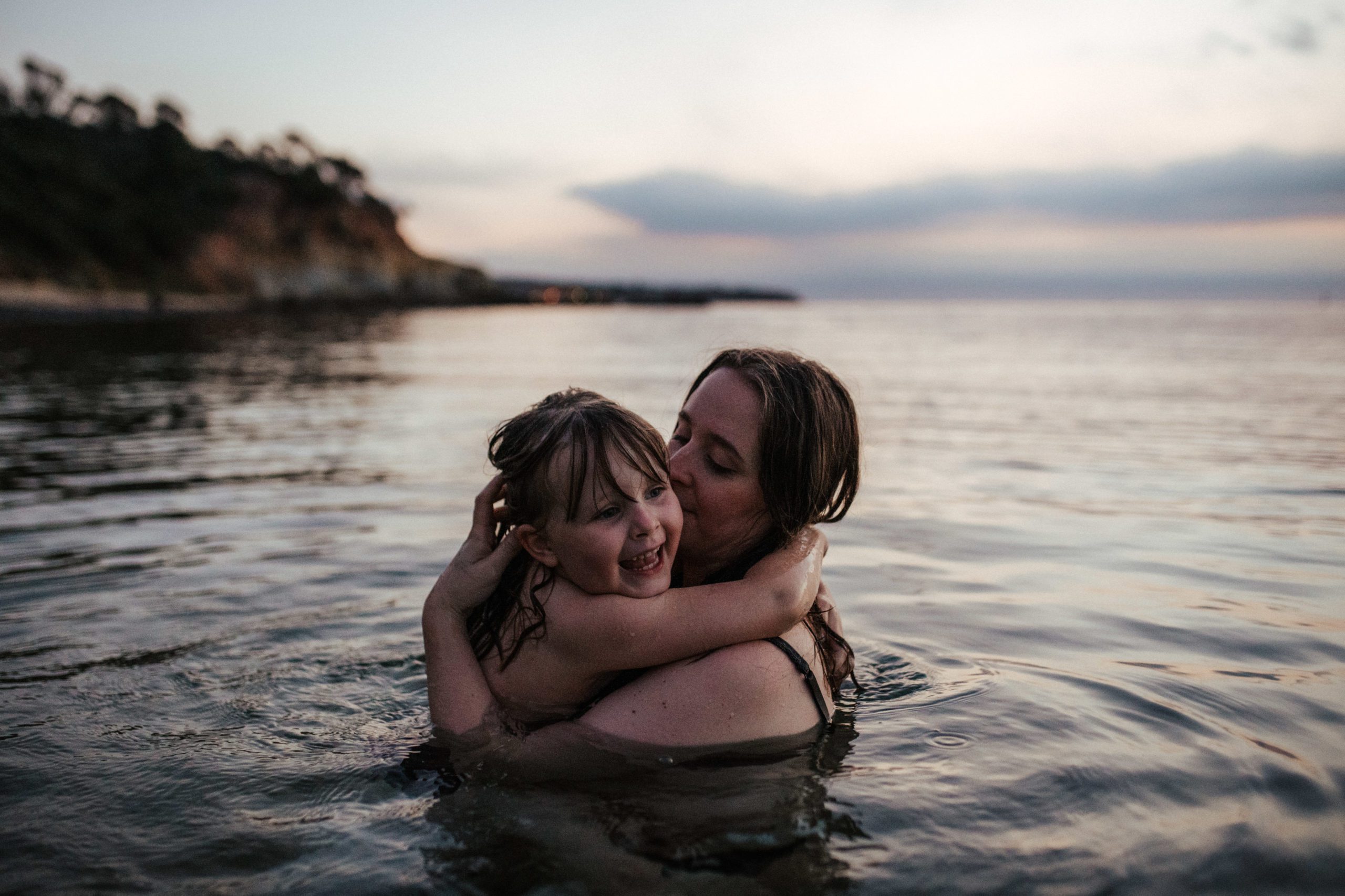 a mother hugs her daughter close in the ocean she has her hands in her hair - it it twilight