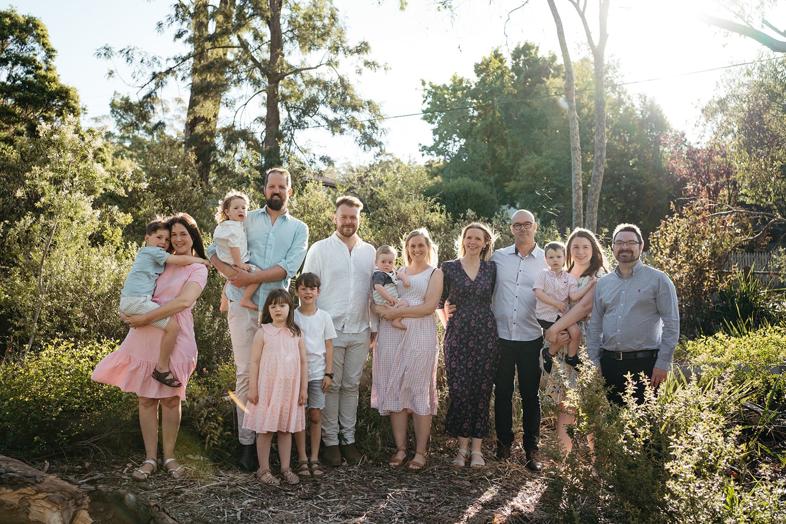 a lighter edit of an extended family backlit, they are wearing pastel colours of pink and blue and are looking at the camera