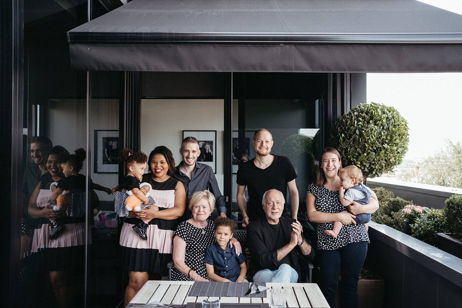 an extended family stands and sits together - they are on a balcony and the dominant colour the are wearing is black and white they are a mixed race family