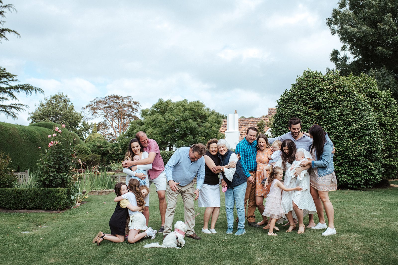 An informal extended family photo with lots of hugging on a green grassy lawn.