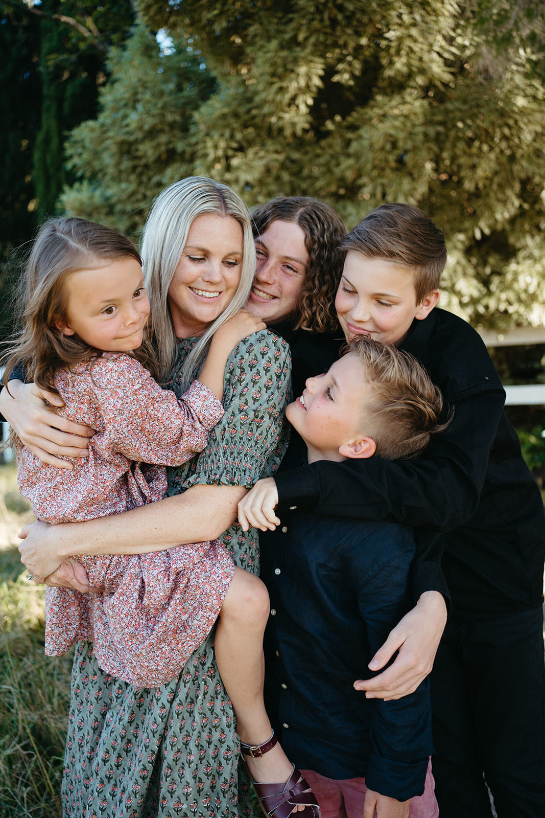 a mother hugs her four children, her youngest daughter is being held and her older boys are hugging all together