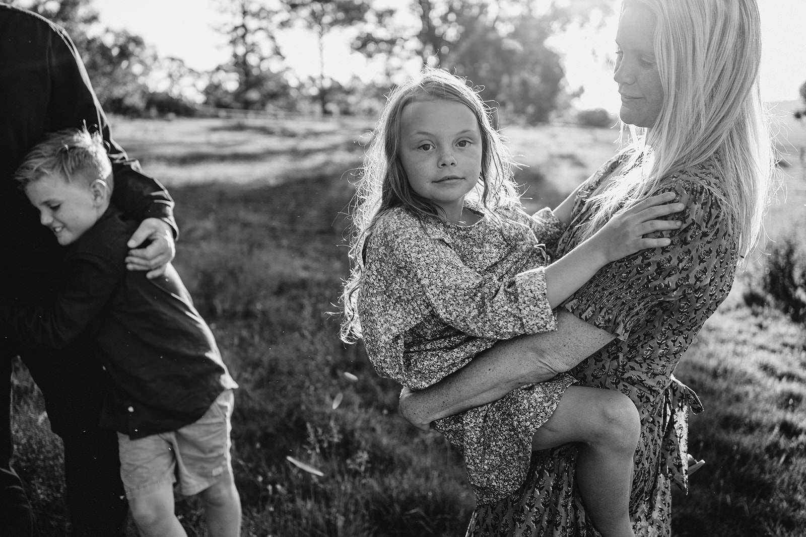 a black and white image of a young girl with her legs wrapped around her mothers waist she is looking at the camera