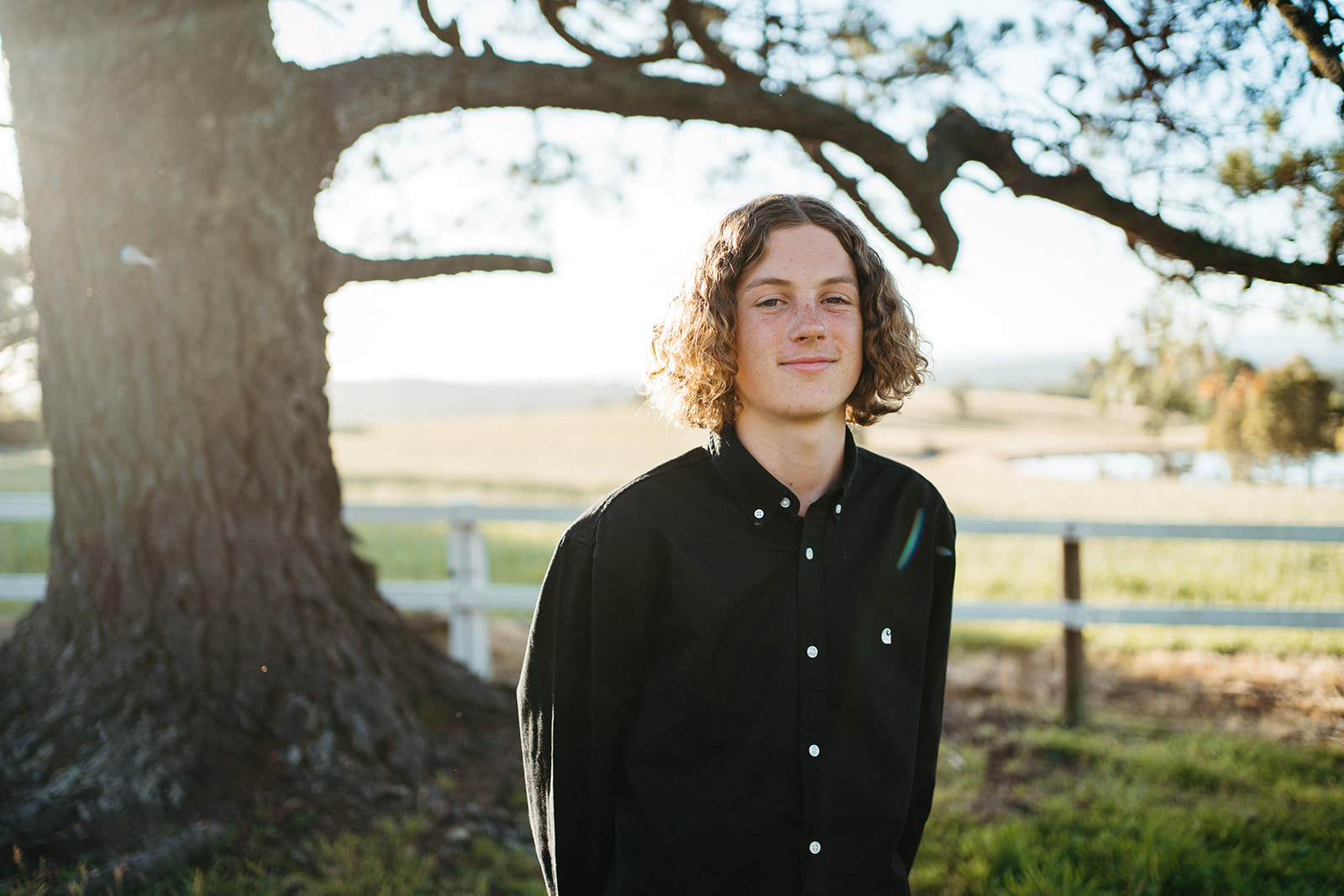 portrait of a teenage boy with curly long hair in a outdoor rural setting