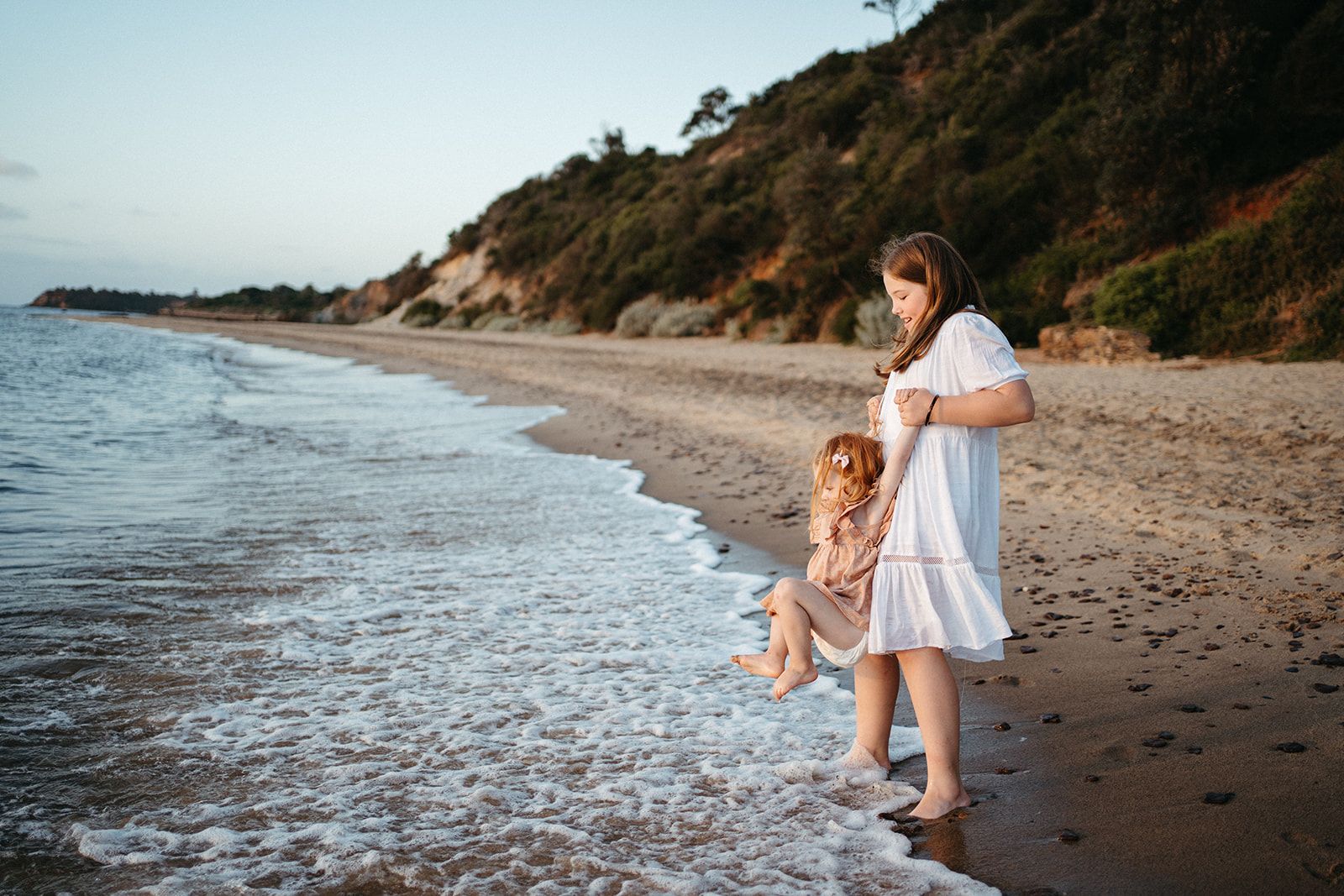 a girl lifts her young sister so her toes don't get caught by the waves