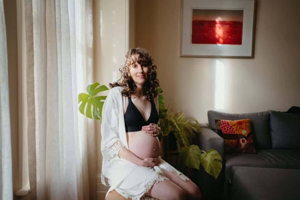 pregnant mother sits in window in a robe