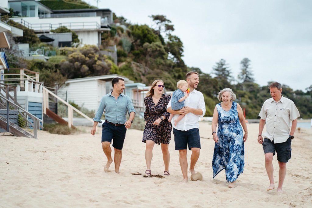 an extended family walk along the beach they are wearing shades of blue and navy
