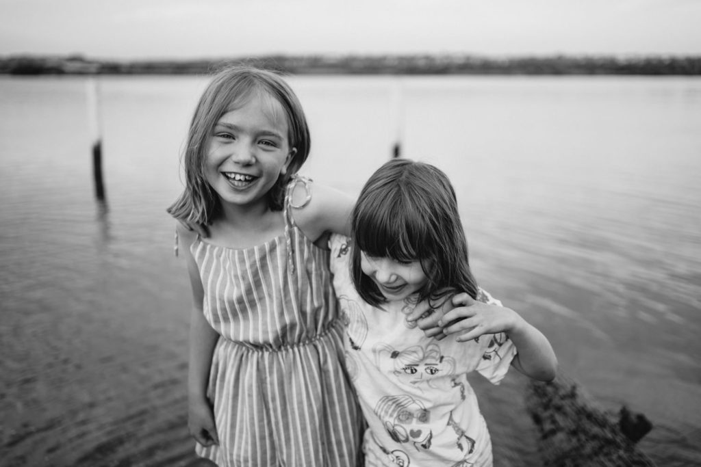 a candid photo of two children with their arms around each other in front of a lake