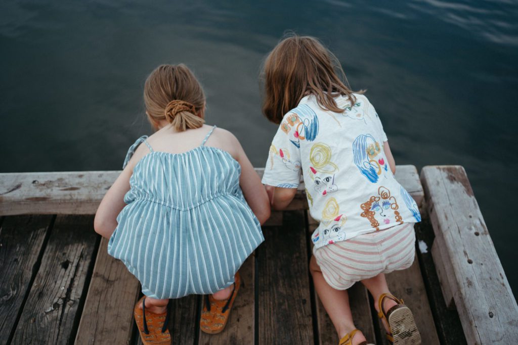 a candid image of two children looking into the water from a pier
