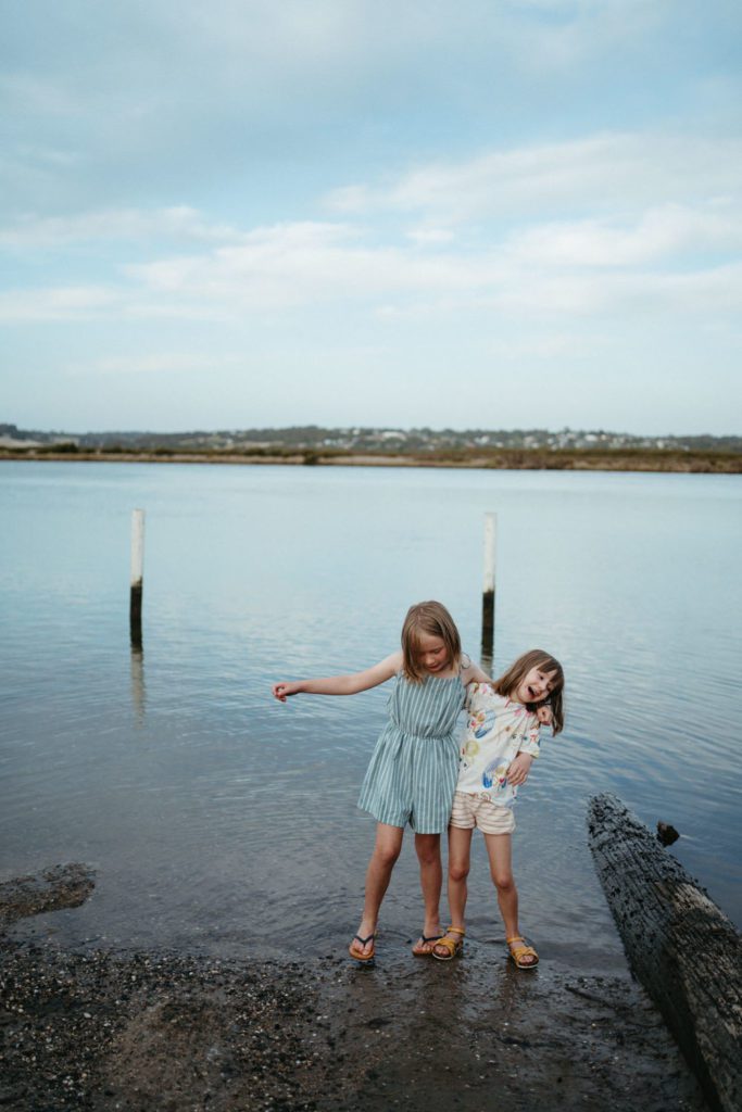 two girls candidly walking at a lake edge with their arms around each other