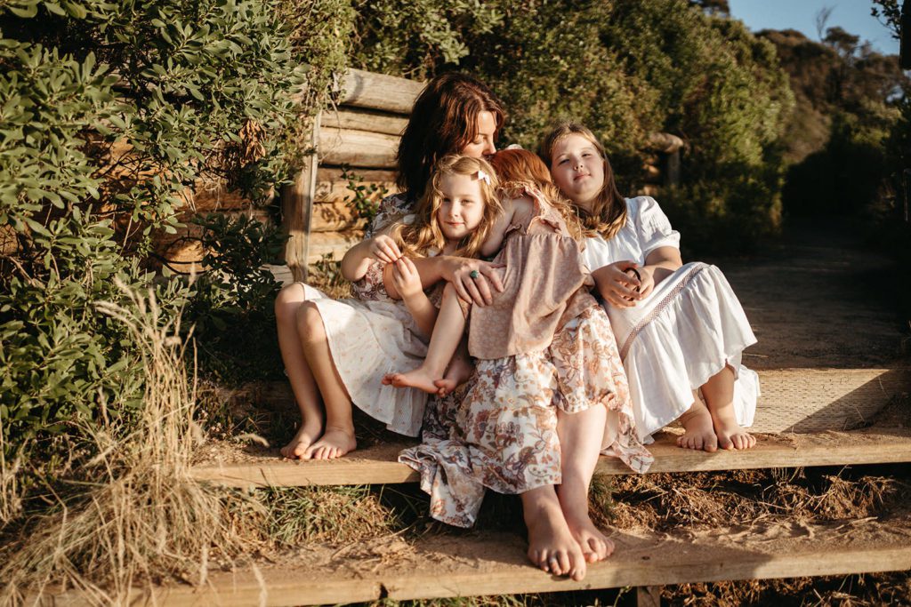 a mother hugs her daughters they are in light dresses with pink tones and varying patterns