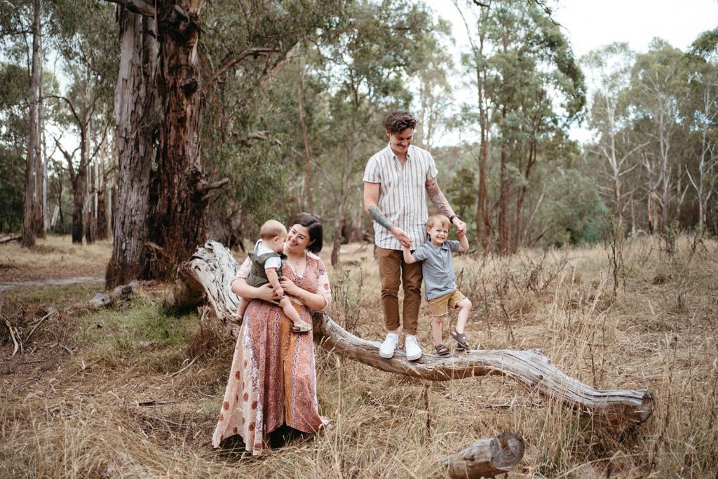 a family in neutral tones but different patterns in bushland in Melbourne the dad and son stand on a log