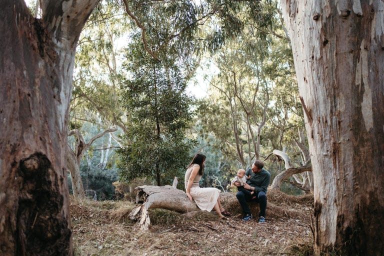 A melbourne couple sit on a fallen gum tree log with their baby