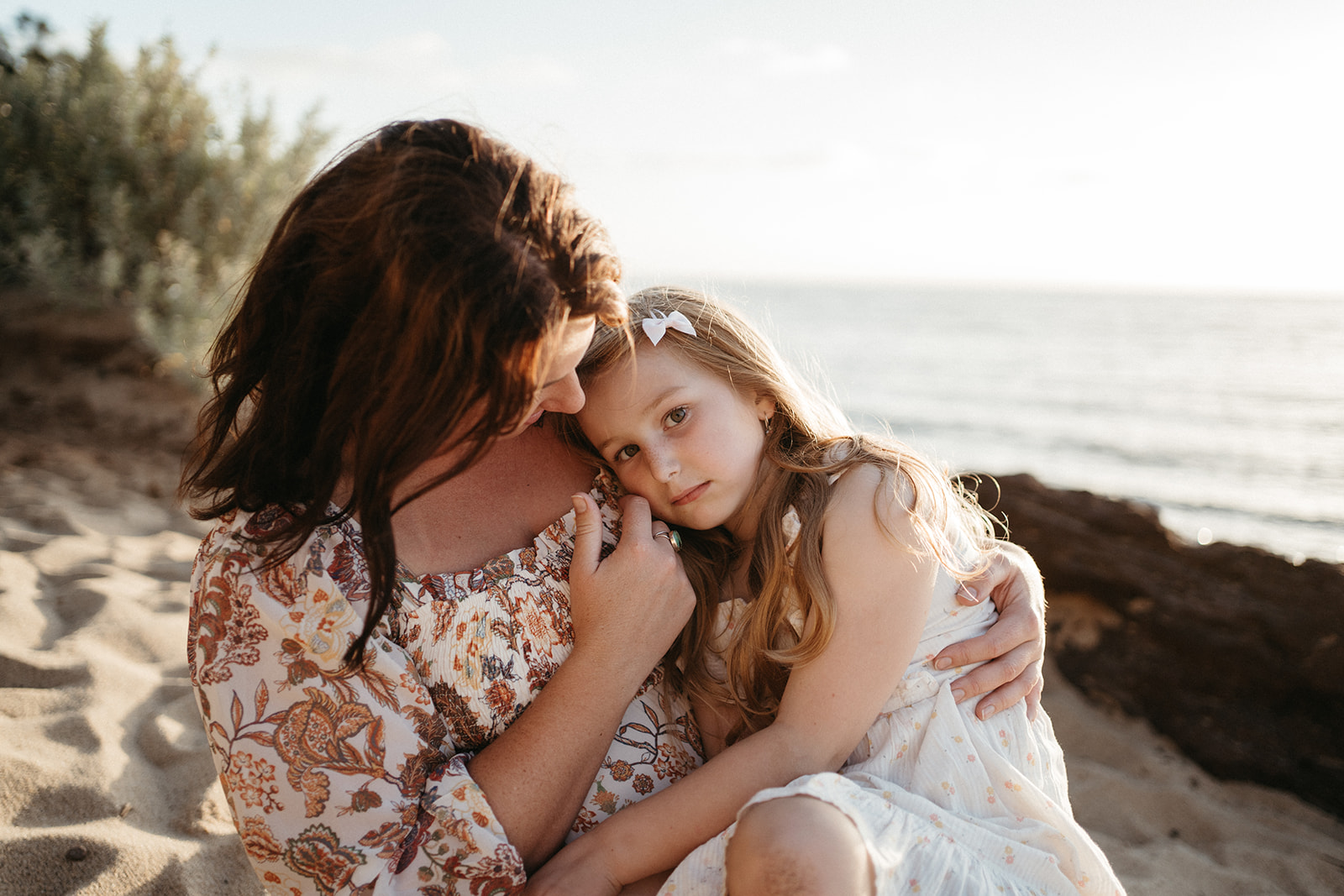 a mother strokes her daughters cheek they are sitting at the beach