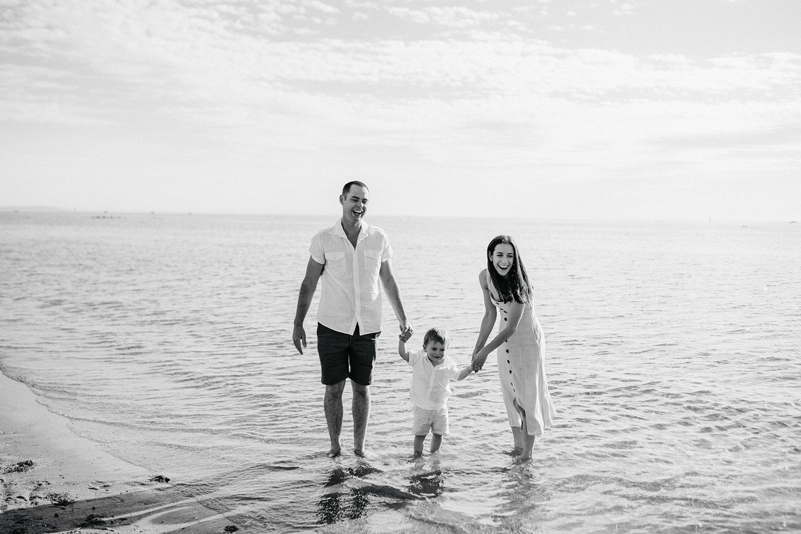 black and white of a family of three laughing at the beach, they are standing in the water