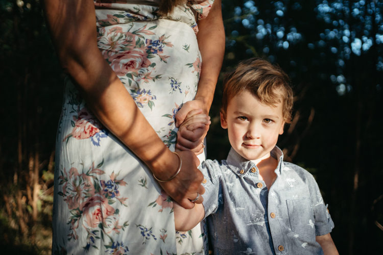 a young boy is held safely by his mothers hand he is standing in dappled light