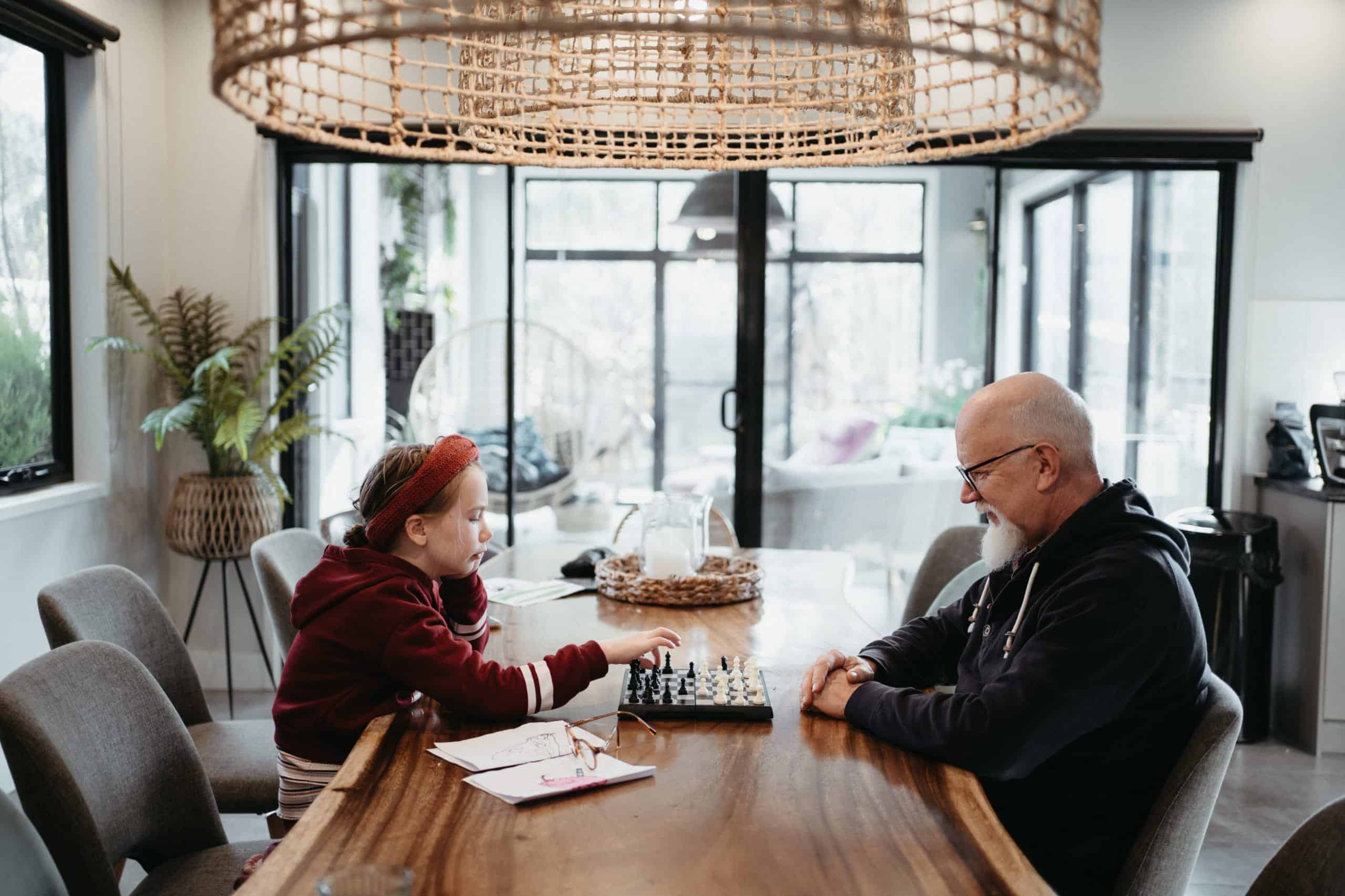 a girl plays chess with her grandfather