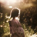 a pregnant woman is backlight with glowing bokeh around her