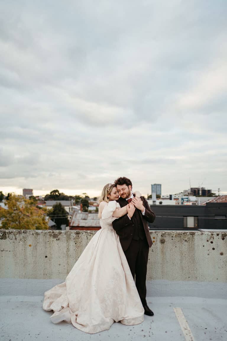 melbourne wedding photography of a couple on a rooftop in the city, the bride has her arms around the groom and they are leaning their heads together
