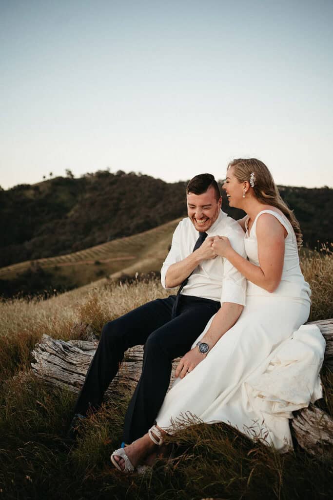 a groom fistbumps his new wife sitting on a log on the top of a mountain in high country victoria