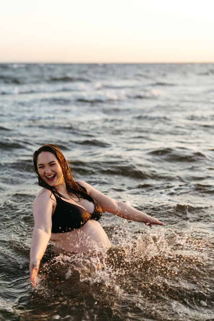 A maternity photograph of a woman laughing in the ocean and splashing the water
