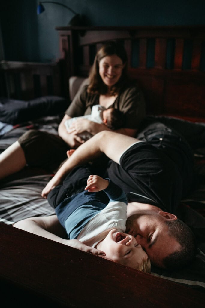 dad hugs toddler, mum with newborn in background