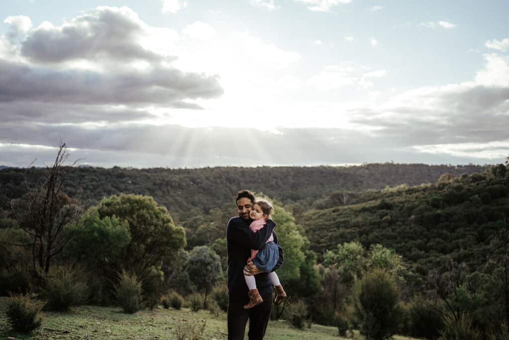 a father hugs his young daughter the sun streams through the clouds behind