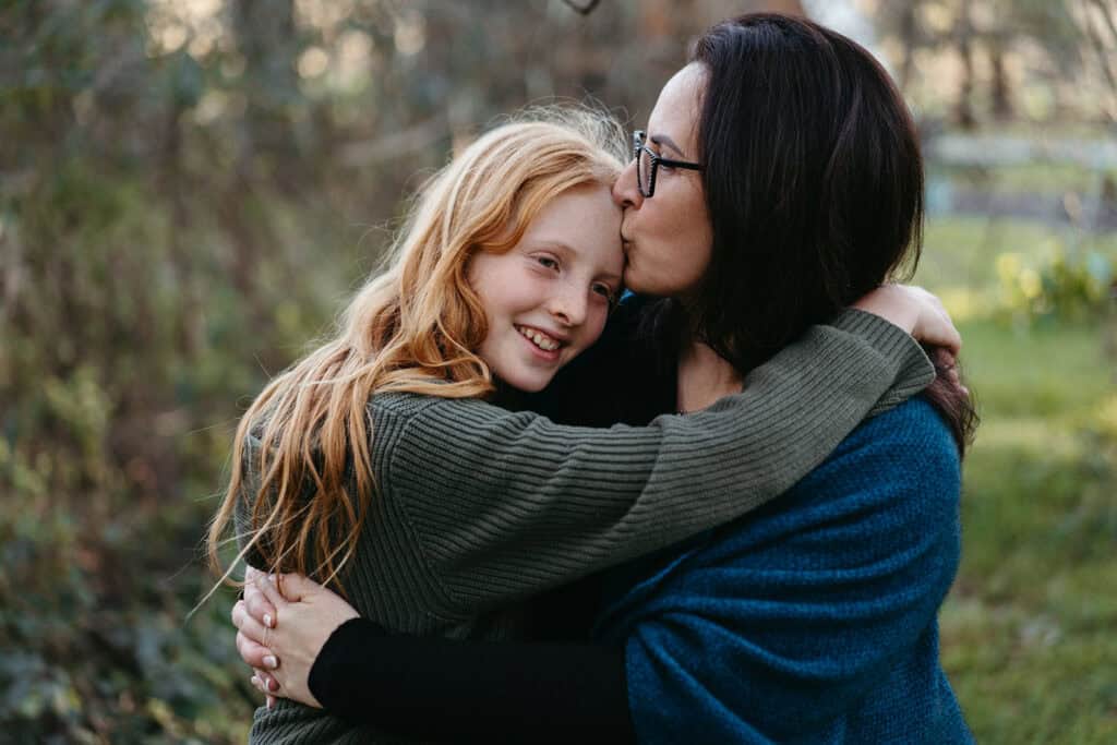 a mother kisses her teenage sons forehead, he has long hair