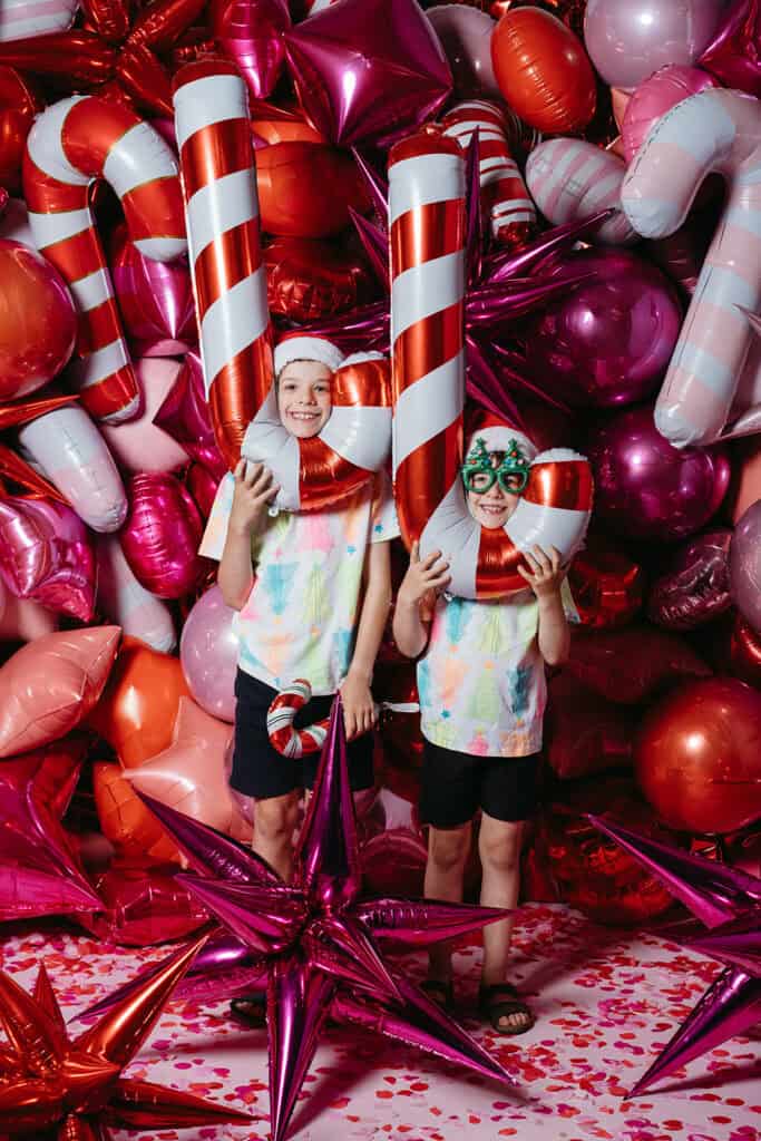 two kids hold upside down candy cane balloons at a Christmas mini session for Poppies for Grace in Melbourne
