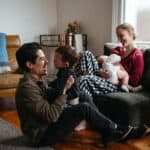 a family in their living room with a young boy and a newborn baby the dad is playing with the boy and the mother is breastfeeding the baby