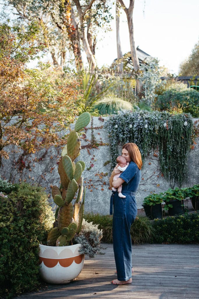 a mother is standing next to a cactus on a back deck holding her newborn baby close