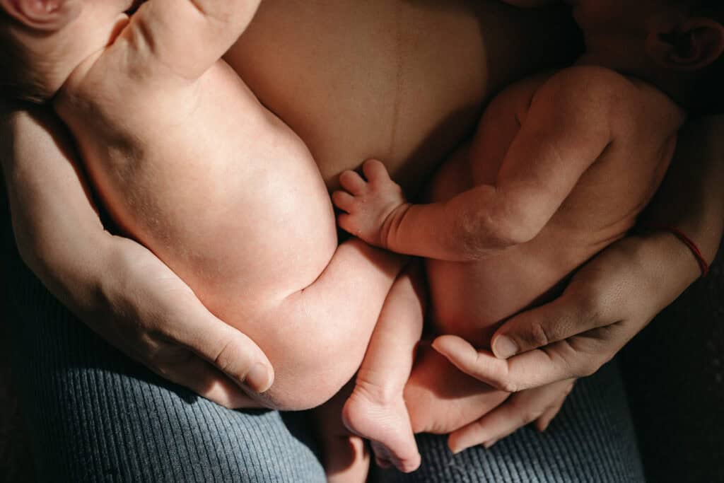 a close up image of a mother holding twins with the line of her pregnant belly