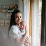 A mother holds her baby and smiles at the camera