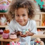 a curly haired boy holds some felt toys and smiles as he leans toward the camera