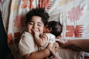 Toddler hugging baby brother during natural newborn photography session in Melbourne, lying on patterned island-style bedding