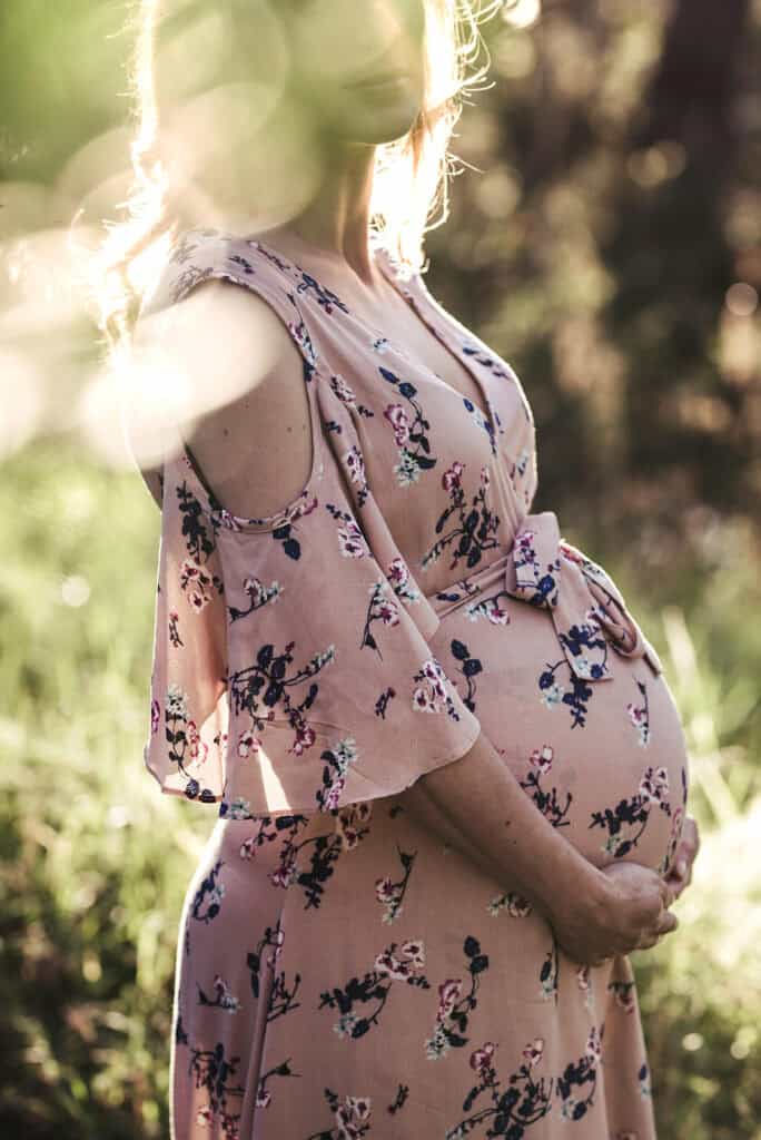 Maternity bump photo of a woman close up with light and leaves infront of her