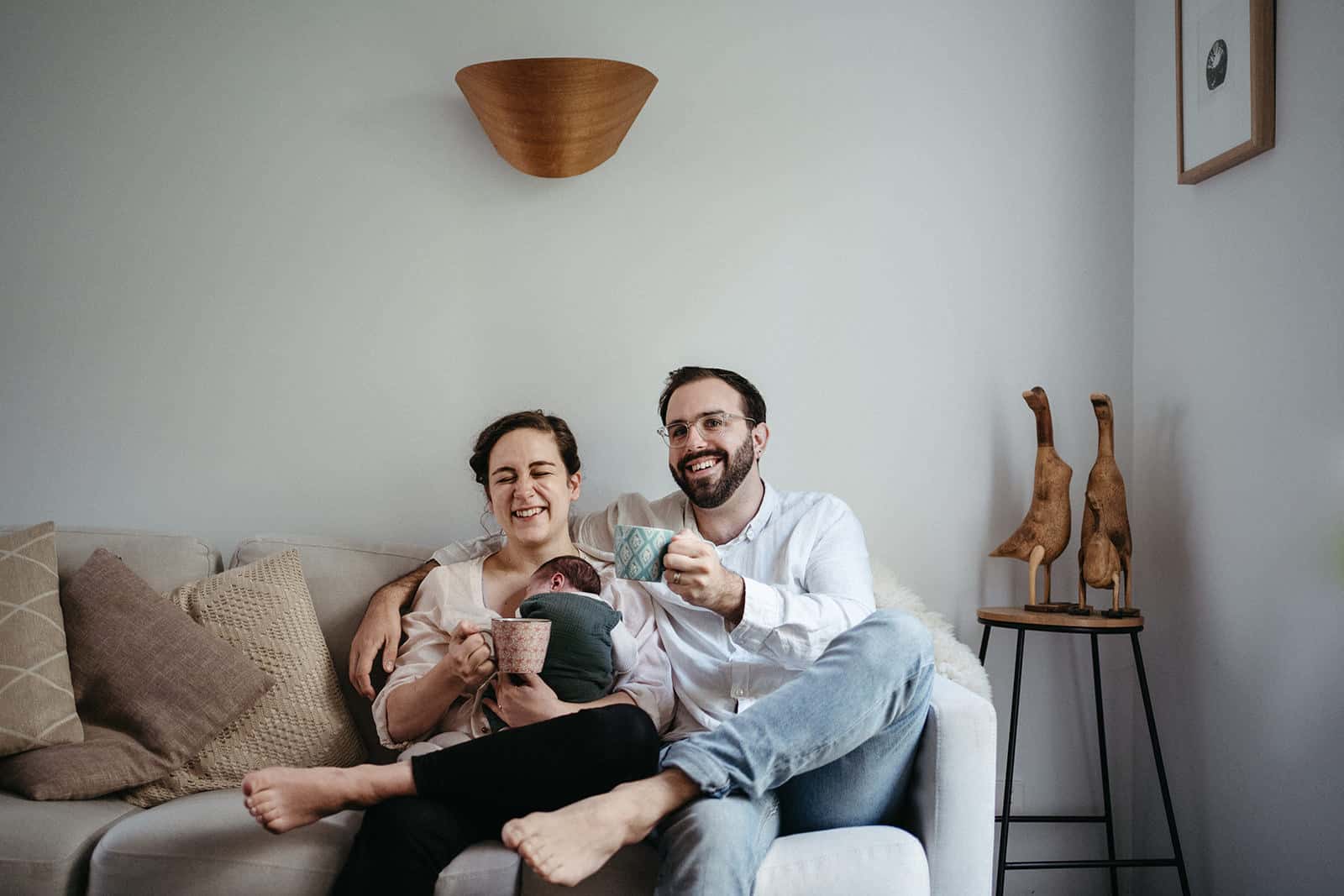 Couple laughing on couch with newborn during relaxed, natural newborn photography session in Melbourne home