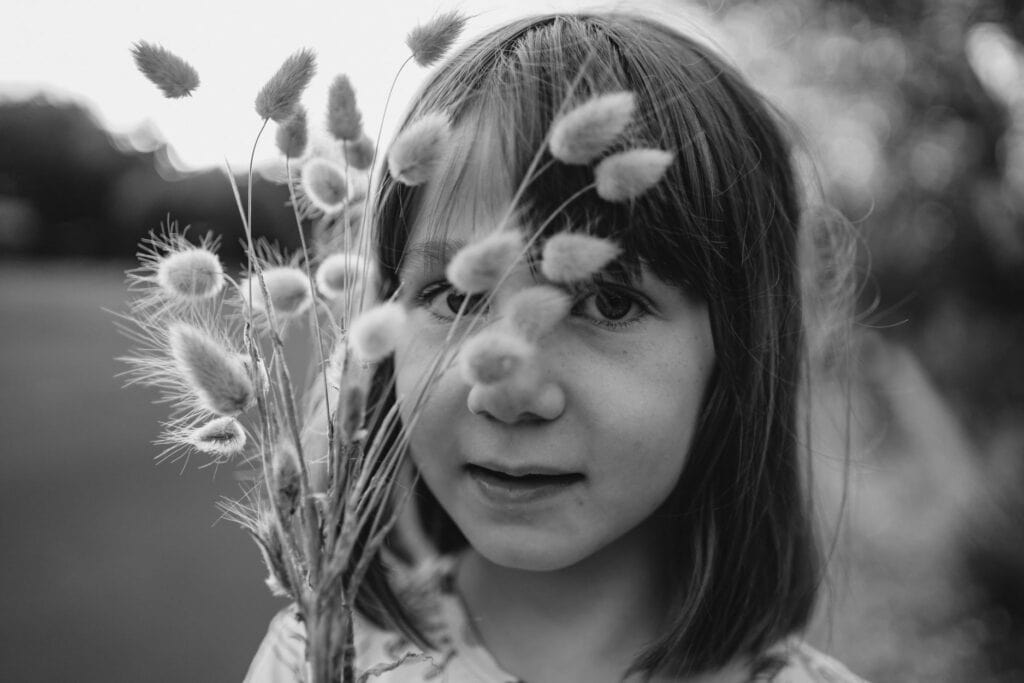 black and white image of a girl holding grass infront of her face