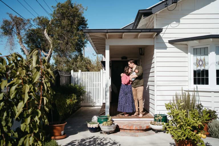 a mother and father holding a newborn stand infront of their melbourne home