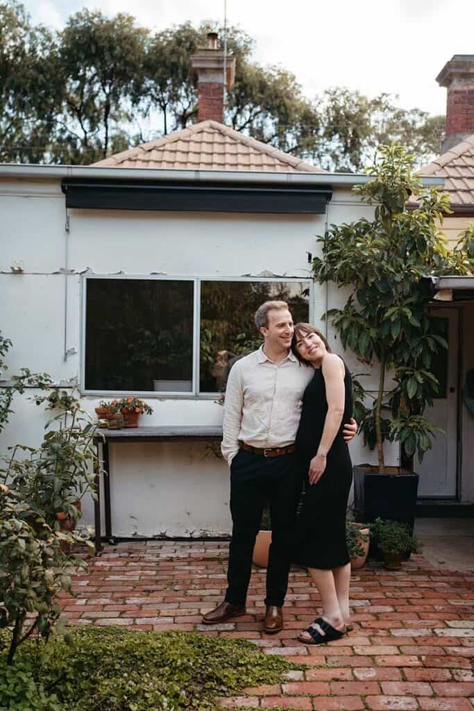 a pregnant couple stands casually in their Melbourne backyard