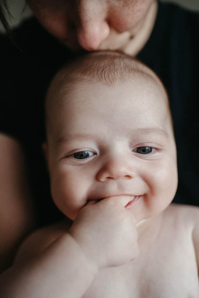 a close up of a mother kissing the top of her six month old babies head he has his hand in his mouth