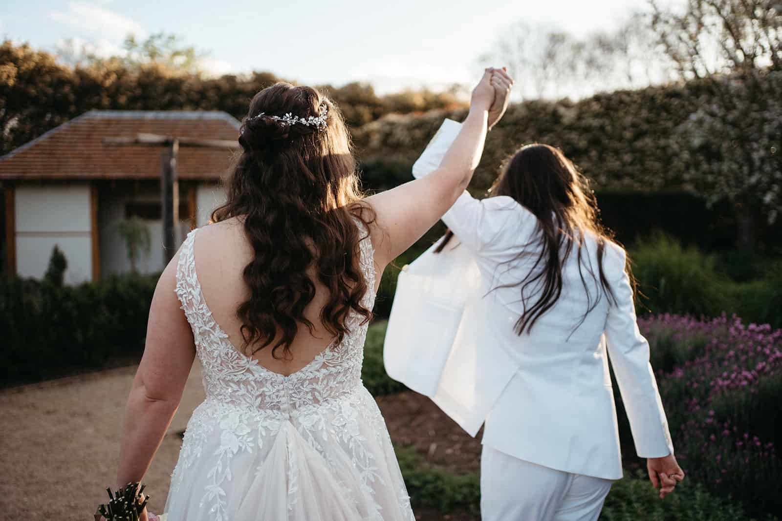back of two brides holding hands up in air