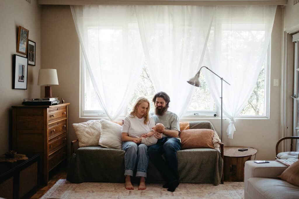 a young couple sits on couch in melbourne apartment with new baby