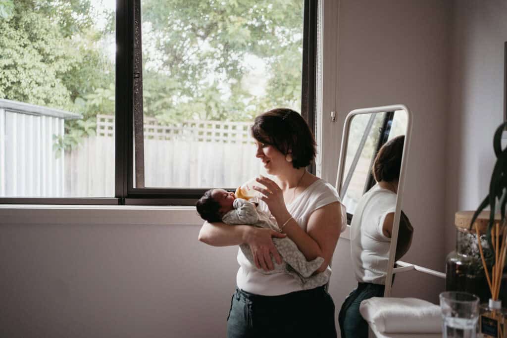 a melbourne postpartum doula holds a newborn baby and feeds the baby a bottle
