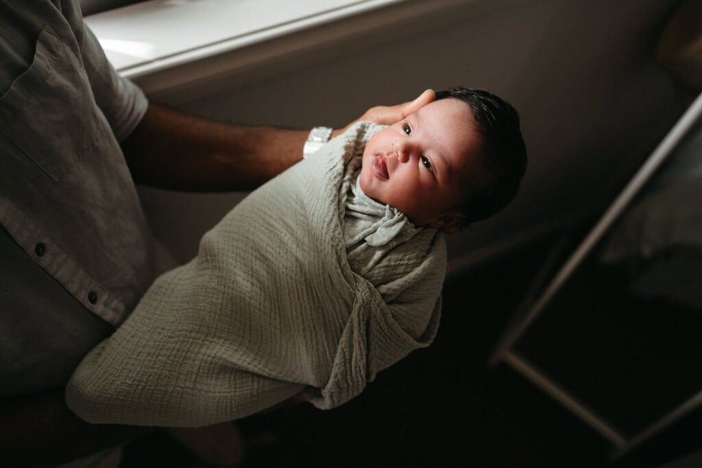 a newborn baby held in window light with a dark background