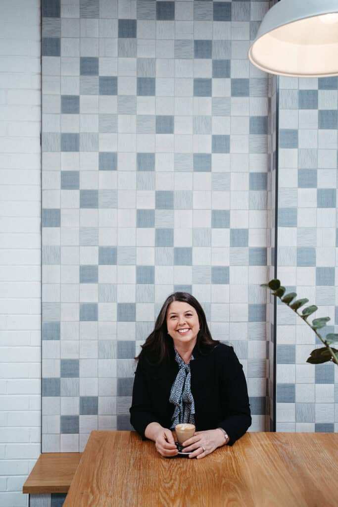 a portrait of a female melbourne professional sitting in a cafe against a blue tile wall
