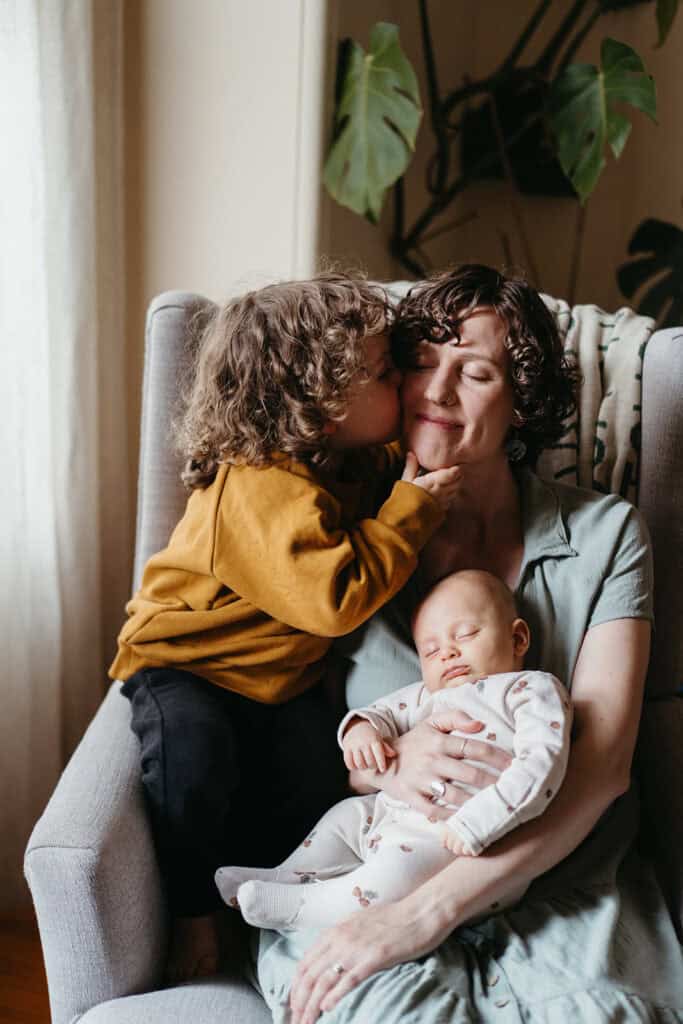 older sibling kisses mother during a newborn session